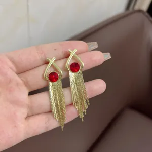 Detail of gold tassel drop earrings with red crystal accents held for size comparison