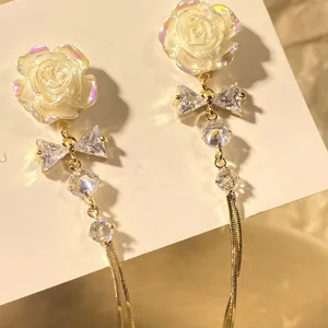 Close-up of elegant white rose earrings featuring a crystal bow and long gold tassel chains