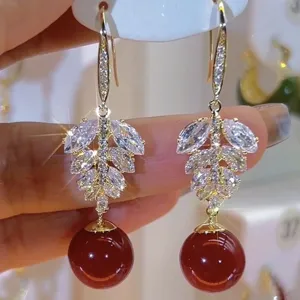 Detailed close-up of sparkling leaf rhinestone earrings with a vibrant red bead drop
