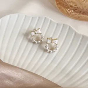Elegant white bow stud earrings with small pearls displayed on a white shell tray