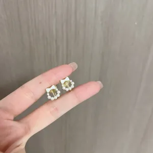 Detailed view of elegant gold stud earrings featuring a white bow and pearl wreath