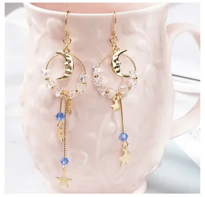 Détail de boucles d'oreilles asymétriques étoile et lune avec perles bleues et cristaux.