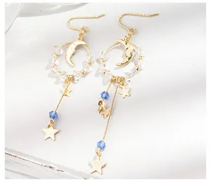 Vue détaillée des boucles d'oreilles asymétriques dorées avec étoiles, lunes et cristaux bleus
