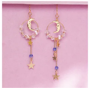 Détail de boucles d'oreilles asymétriques à pompons dorés avec perles, motifs lune et étoile