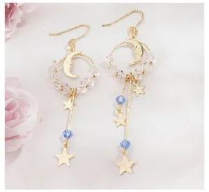 Détail de boucles d'oreilles asymétriques en or avec étoiles, lune et perles de cristal bleu.