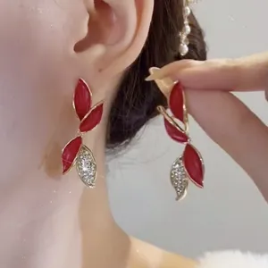 Dettaglio di eleganti orecchini a foglia rossa con strass scintillanti e finitura oro