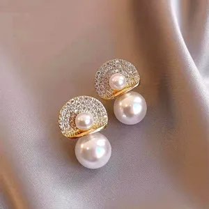 Close-up of elegant gold-toned pearl earrings with micro-pave zirconia details on satin