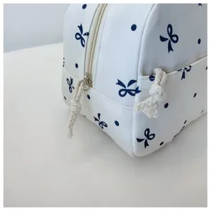 Elegante bolsa de cosméticos blanca con estampado de lazos azules y cremallera práctica.