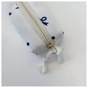 Primer plano detallado de estuche blanco de lona con topos azules y un bonito lazo con cremallera.
