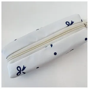 Detalle de estuche de lona blanca con estampado de lazos azules y lunares con cremallera.