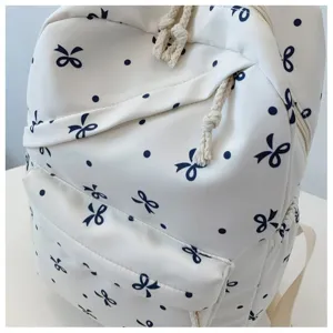 Detalle de una mochila de color crema claro con lazos azul oscuro y lunares bonitos.