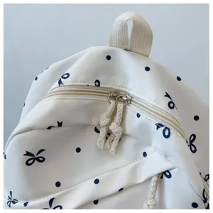 Primer plano detallado de la mochila blanca crema con bonitos lunares y lazos negros.