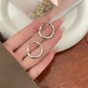 Close-up view of minimalist polished silver hoop earrings held by a hand for scale