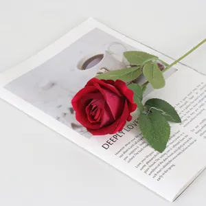 Primer plano de una rosa artificial de terciopelo rojo sobre una página de revista decorativa.