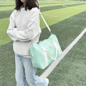 Outdoor detail view of a large capacity light green textured travel duffel bag with shoulder strap.