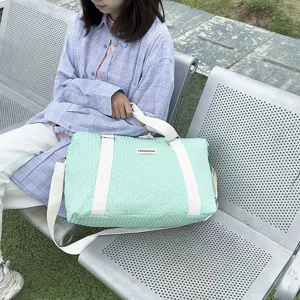 Detailed view of mint green quilted travel tote bag with white straps in outdoor scene.