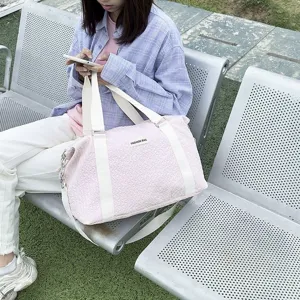 Outdoor lifestyle close-up of a pink quilted travel duffel bag with white canvas straps.