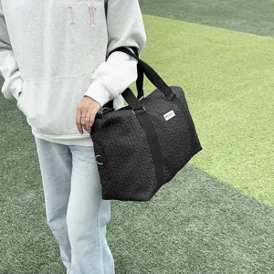 Detail shot of black quilted duffle bag outdoor scene showing handle and textured fabric.