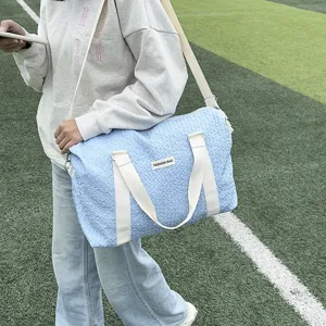 Outdoor scene detail shot of a light blue quilted travel duffel bag with white straps.
