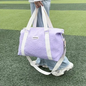 Outdoor detail shot of a large purple quilted travel duffle bag with white straps.