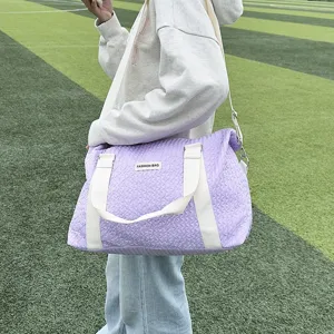 Detail view of the large purple quilted travel duffel bag with white straps for sports.