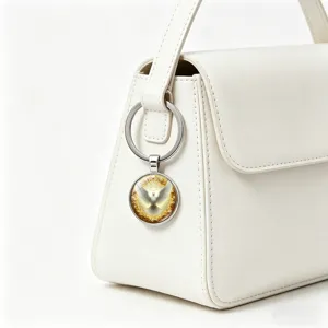 Close-up of a silver dove pendant keychain attached to a white leather handbag.