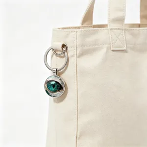 Detailed view of a green dragon eye glass cabochon keychain hanging on a canvas tote bag