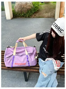 Detailed view of a large purple checkered travel bag held by a model in an outdoor setting