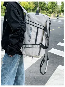 Back view of a large gray grid travel bag carried outdoors on a street background.