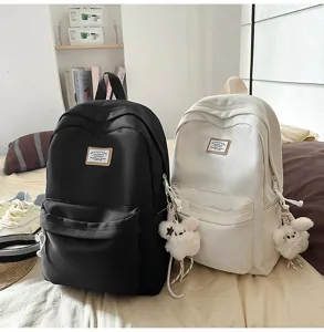 Detailed view of canvas casual school backpacks in black and white with cute plush pendants.