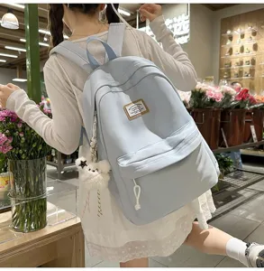 Lifestyle detail shot of light blue school backpack with cute bear pendant in store setting.