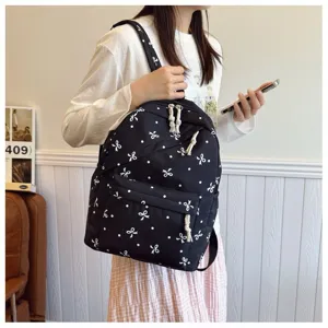 Detalle de la mochila negra con elegantes patrones de lazos blancos y bolsillo frontal útil.