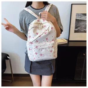 Vista detallada de una mochila escolar blanca informal con un encantador patrón de lazos rojos.