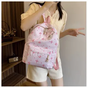 Mochila rosa con estampado de lazos detalle que muestra bolsillo frontal y tela suave.