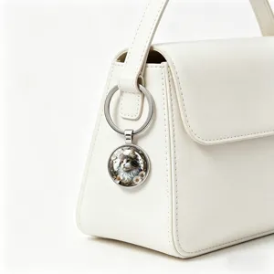 Detail shot of a round cat glass cabochon keychain hanging on a white elegant leather handbag.