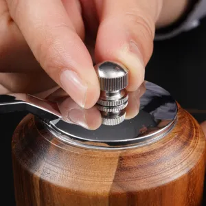 Close-up detail of manual wooden pepper grinder metal adjustment knob and handle operation.