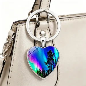 Nahaufnahme eines herzförmigen Schlüsselanhängers mit Nordlicht-Wald-Print an einer Handtasche