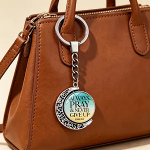 Close-up view of motivational rotating moon keychain with bible verse hanging on a leather bag