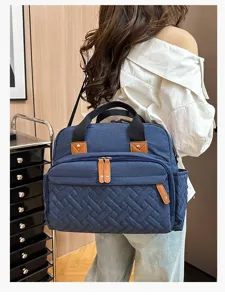 Back view of a stylish large capacity blue quilted diaper bag worn by a model outdoors