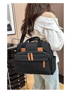 Rear view of a stylish black quilted diaper bag with brown leather accents on a model