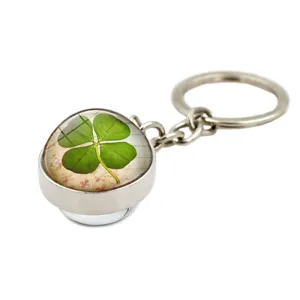 Detail view of a metal keychain with a green four-leaf clover under a glass dome.
