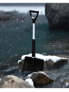 Gros plan d'une pelle à neige en plastique avec manche télescopique dans la neige.