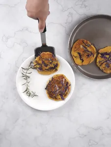 Detail view of a black silicone kitchen spatula flipping a savory pancake on a clean white plate.