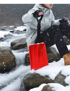Gros plan d'une pelle à neige en plastique rouge utilisée dans un paysage hivernal enneigé