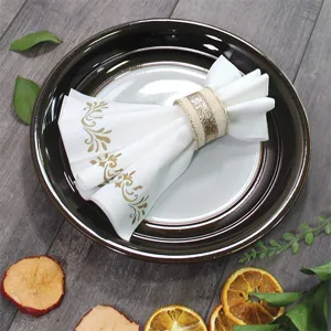 Detailansicht der weißen Einwegserviette mit Goldfolien-Blumenmuster auf einem dunklen Teller