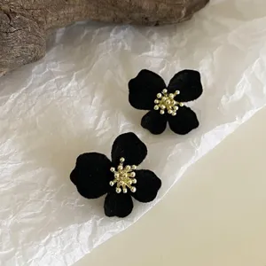 Macro view of black flocked flower earrings with gold-tone centers on textured paper
