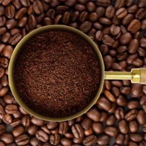 Detail of gold-plated coffee measuring scoop with wood handle over roasted beans