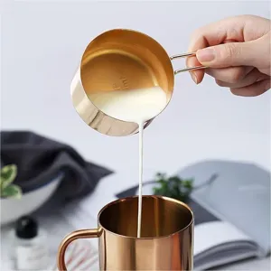 Detailaufnahme des goldenen Messbechers aus Edelstahl beim Eingießen von Milch zum Backen.