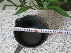 Close-up of 16cm cast iron milk pot showing diameter measurement with a metal tape measure