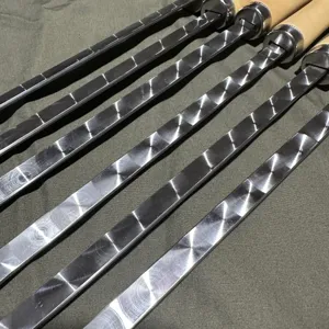 Close-up of flat stainless steel BBQ skewers with unique circular patterns and wooden handles.